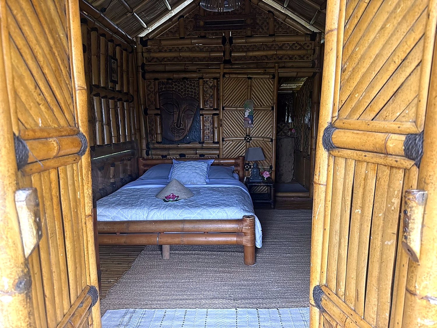 Chambre de la Maison Thaï 2 vue depuis les portes en bambou, lit double et tête de lit sculptée