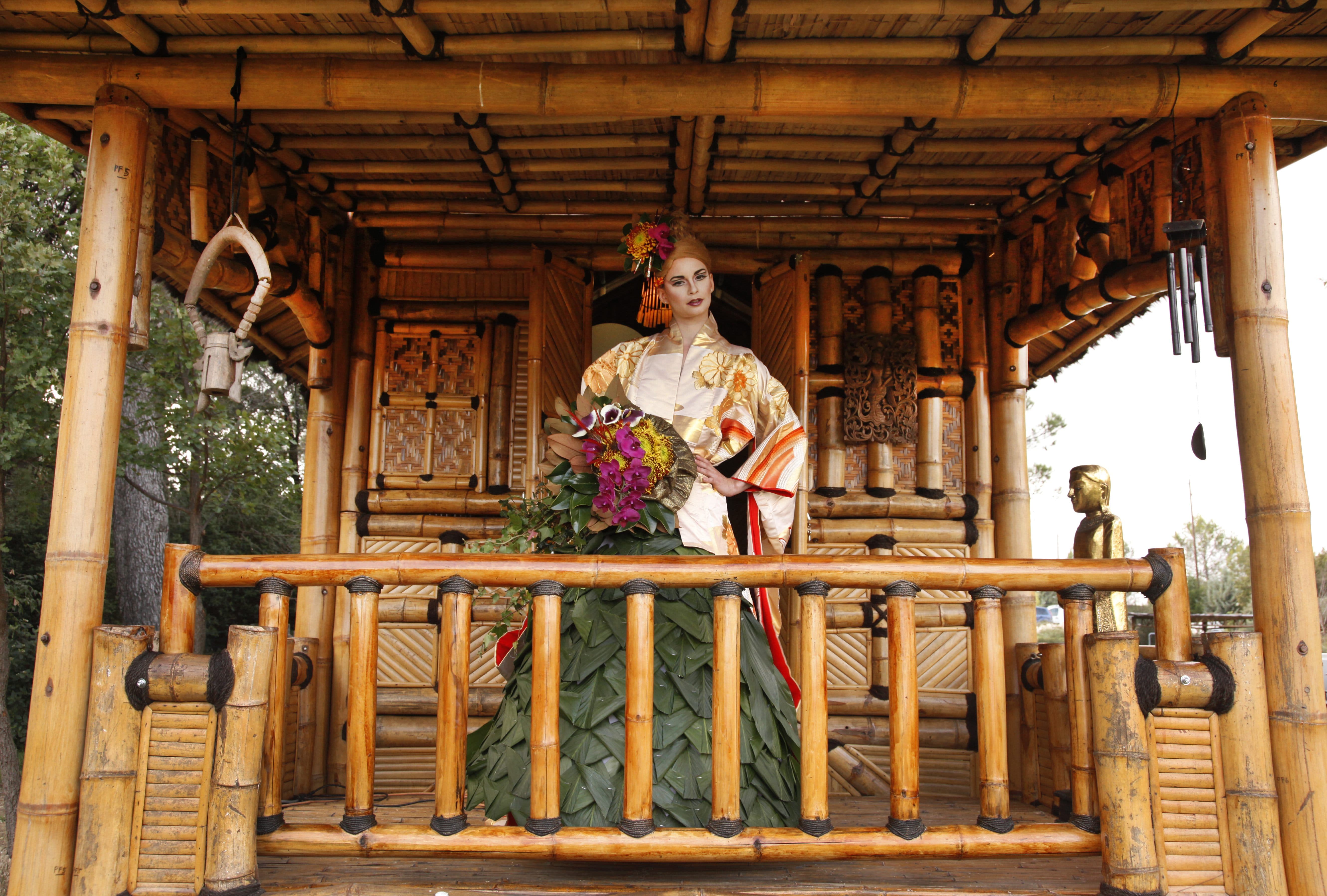 Mannequin en costume thaï doré, bouquet en main, sous le sala en bambou.